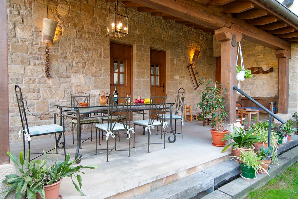 Porche de El Pajar con mesa, sillas y plantas junto a la fachada de piedra