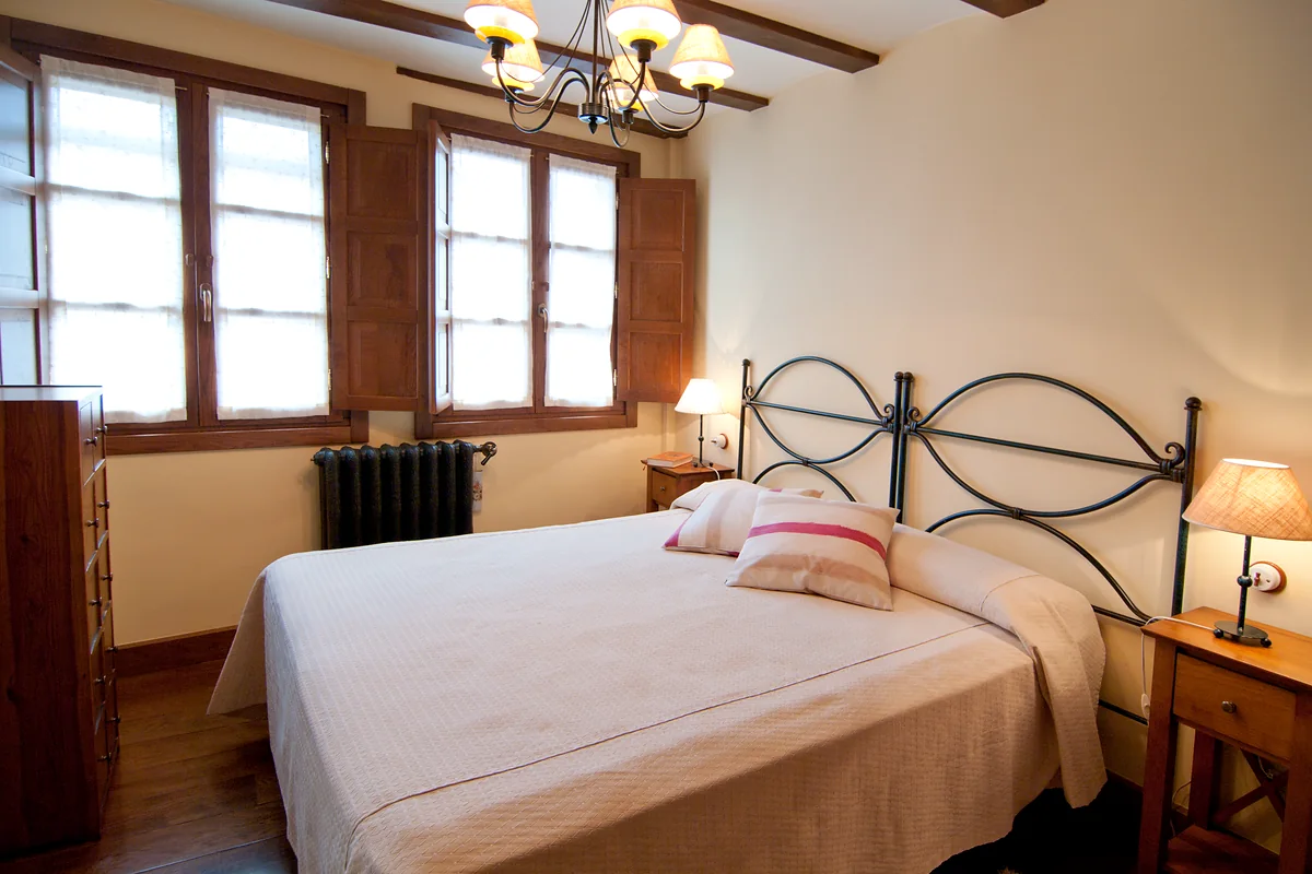 Dormitorio de El Pajar con cama doble, ventanas y vigas de madera